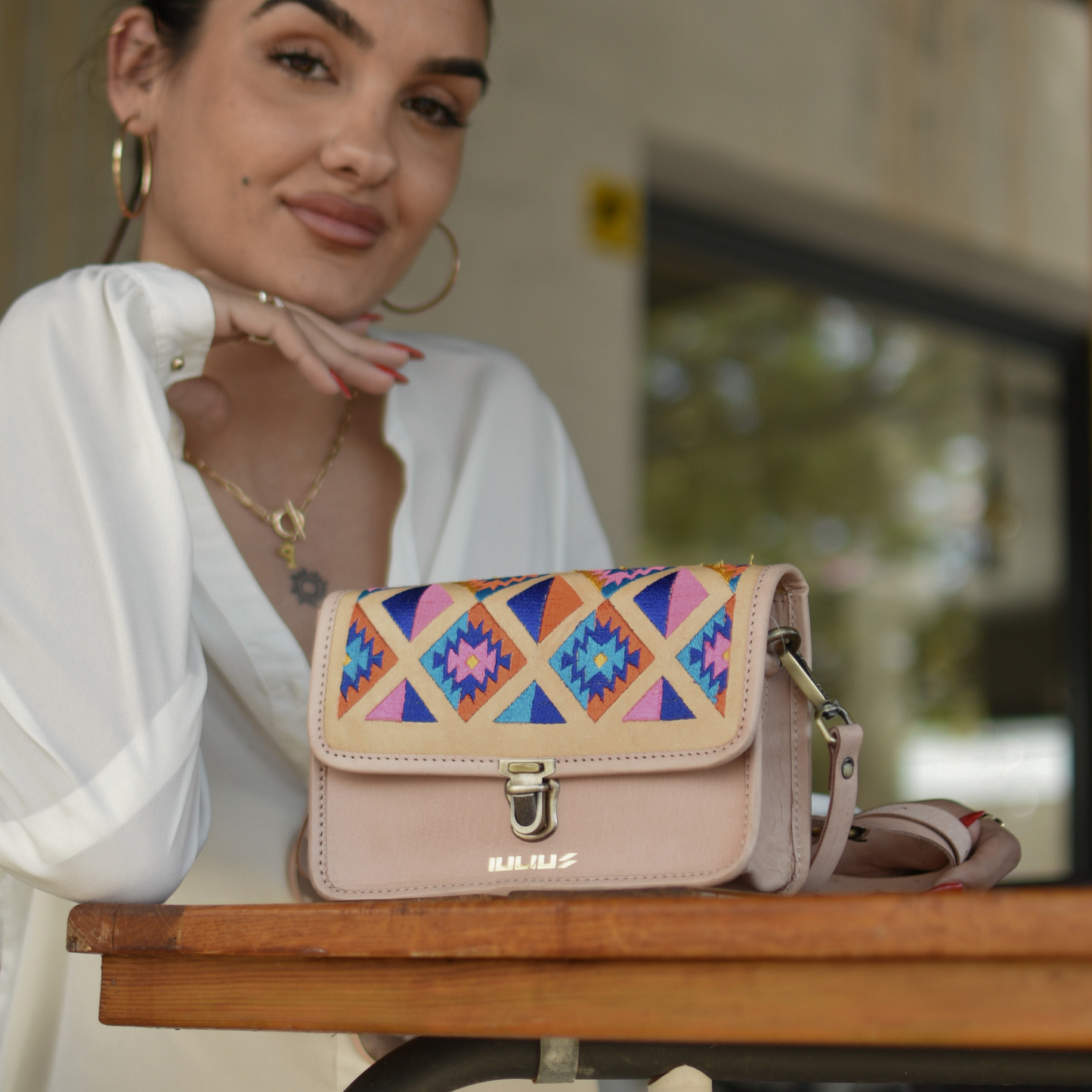 Modelo femenina mostrando bolso IULIUS con estilo étnico sobre una mesa de terraza