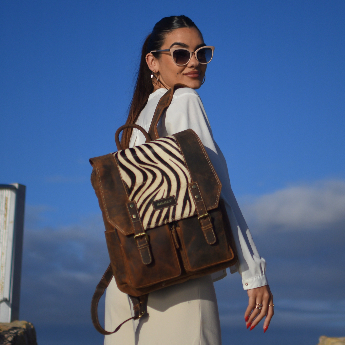 Mujer elegante llevando mochila IULIUS de cuero y piel natural – fondo cielo azul